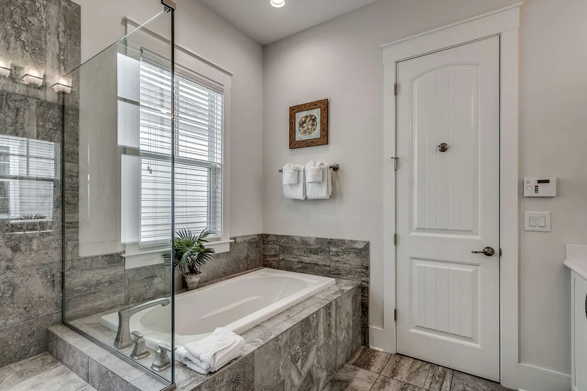 A luxurious bathroom with a freestanding bathtub, large glass-enclosed shower, decorative wall art, a window pouring in natural light, and plush towels on a rack. The space feels tranquil and spa-like, ideal for relaxation and self-care.