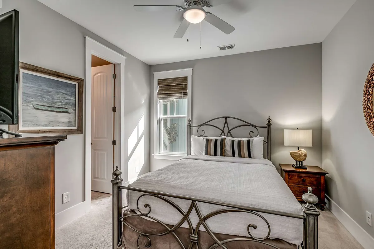 A tranquil bedroom featuring a plush bed adorned with decorative pillows, a wooden nightstand, tasteful artwork on the wall, and a window letting in gentle natural light. The setting feels restful and private, ideal for unwinding.