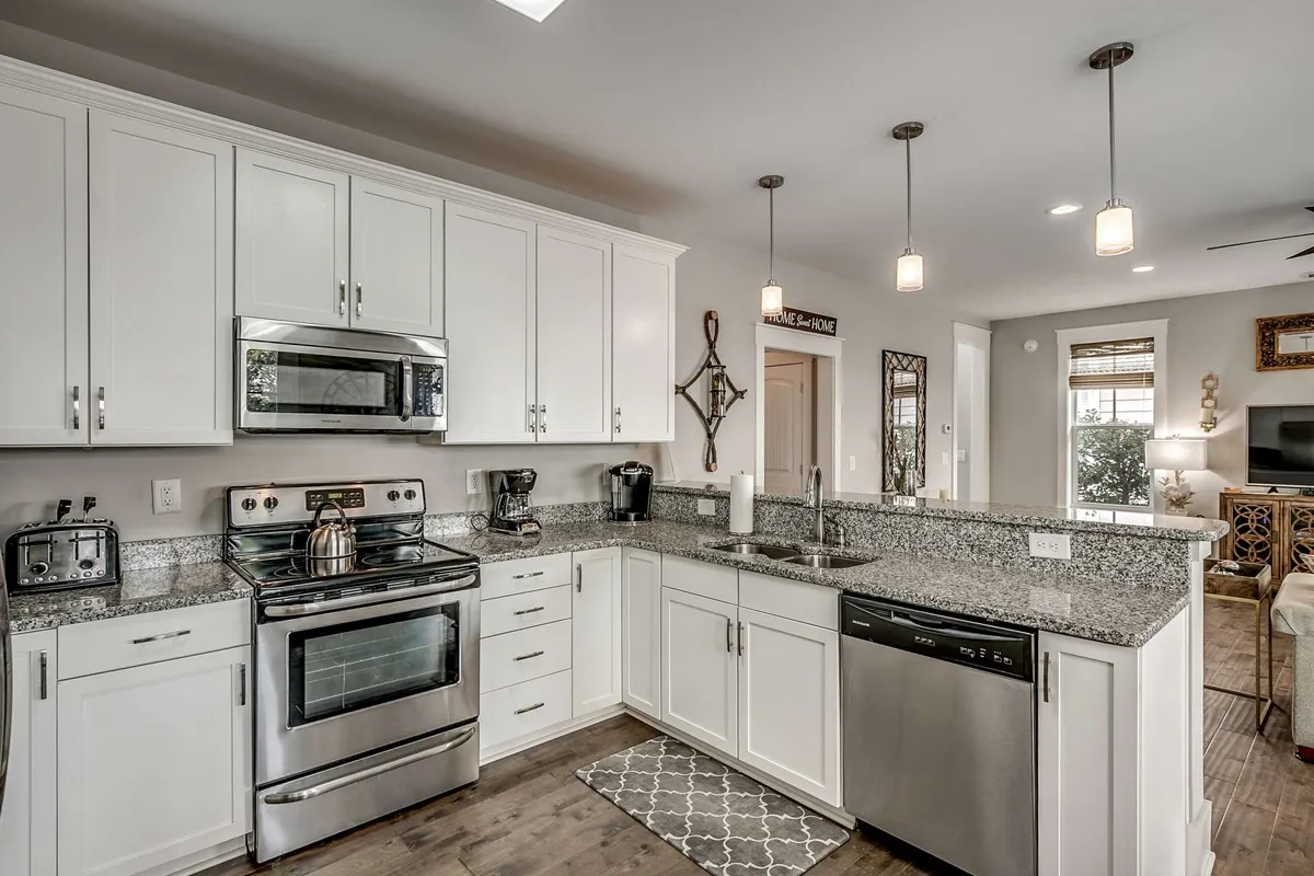 A modern kitchen with granite countertops, stainless steel appliances, a spacious island, pendant lighting, and a decorative mirror. The space is designed for entertaining, with plenty of room for cooking and interacting with guests.