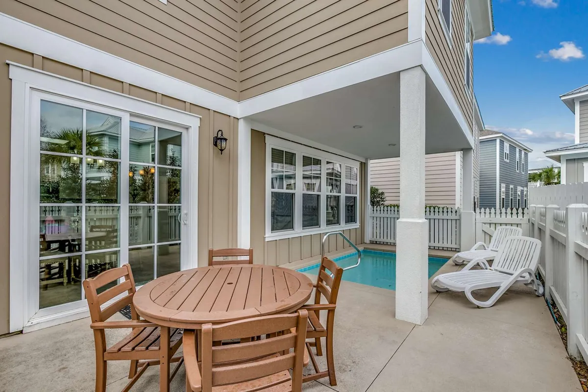 A sunlit patio features a glistening private swimming pool surrounded by a secure fence. There are comfortable lounge chairs for sunbathing, a spacious outdoor dining table set for meals, and a BBQ grill nearby. The ambiance suggests a perfect setting for relaxed poolside afternoons, al fresco meals, and casual gatherings with family or friends.