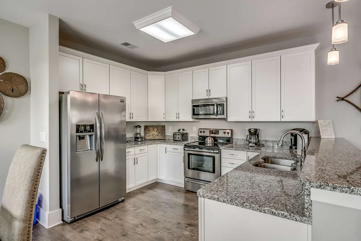 The image highlights a modern kitchen featuring stainless steel appliances, granite countertops, and a spacious kitchen island. The layout is open and inviting, designed for multiple people to gather, cook, and socialize comfortably.