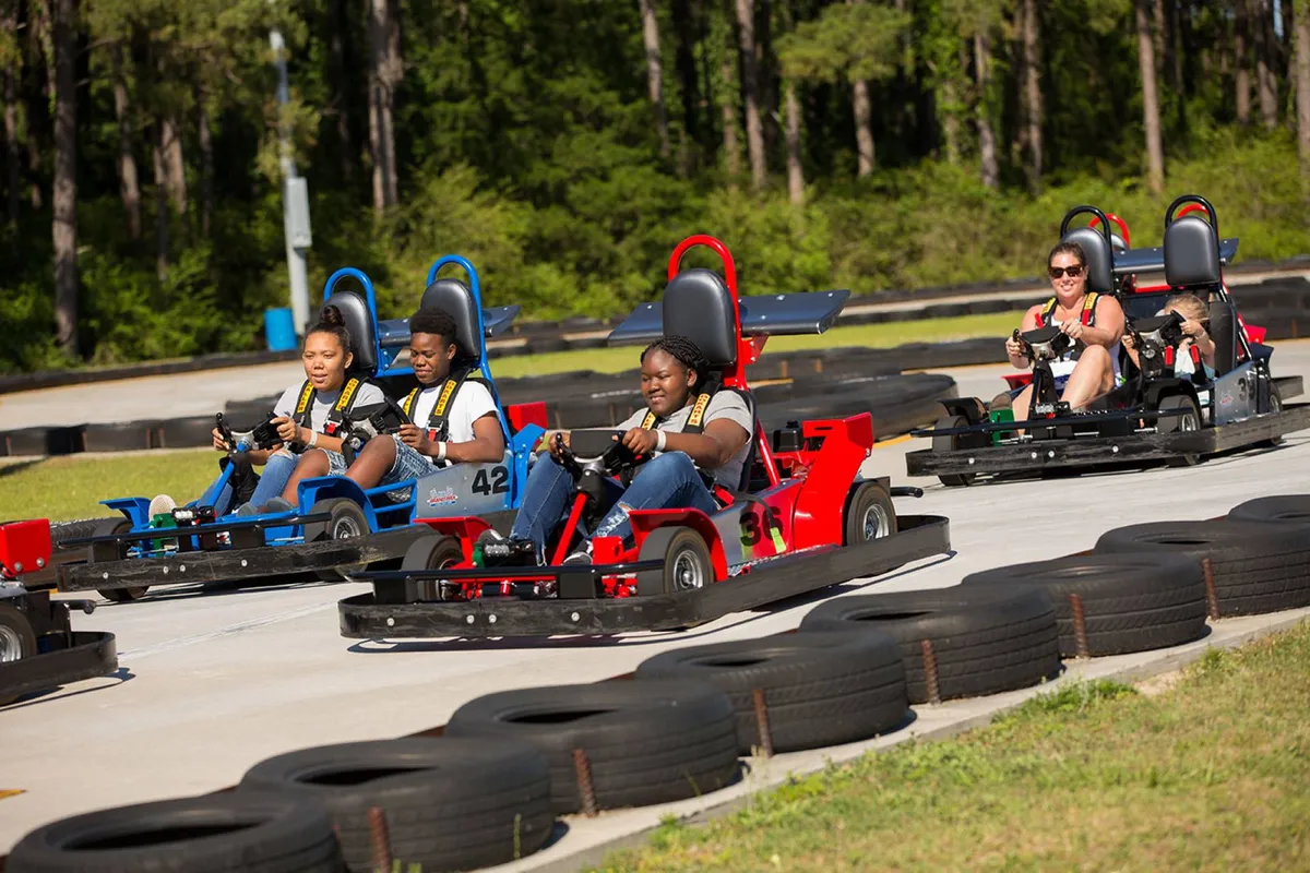 An outdoor go-kart racing scene, featuring go-karts speeding around a track with participants of various ages and onlookers cheering. The image captures the energy and fun of family-friendly competition.