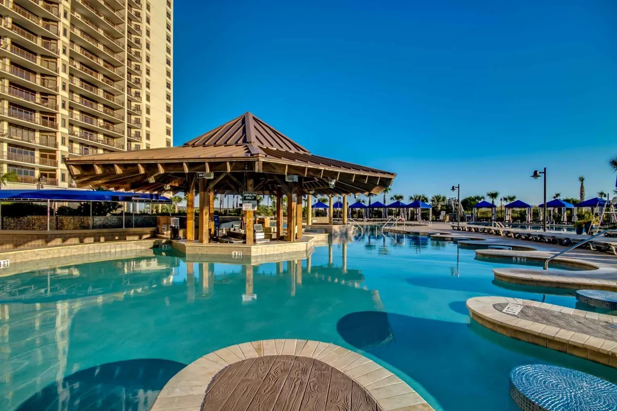A vibrant pool setting with a spacious pool, a shaded cabana, lounge chairs, and swaying palm trees. The area suggests a lively yet relaxing atmosphere, perfect for socializing, sunbathing, or enjoying a poolside drink.