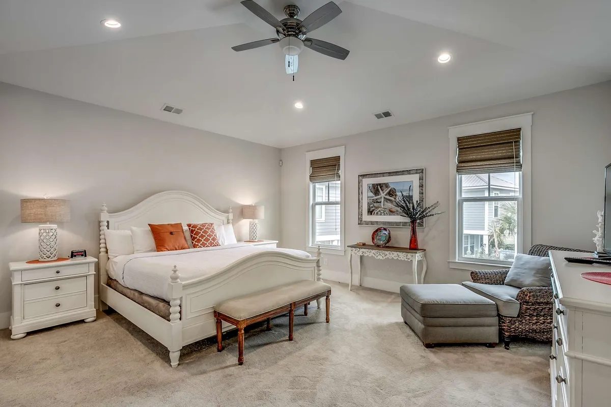 An inviting bedroom with a comfortable bed, flanked by nightstands and cozy seating area. Large windows bring in ample daylight, and decorative details contribute to a soothing atmosphere.