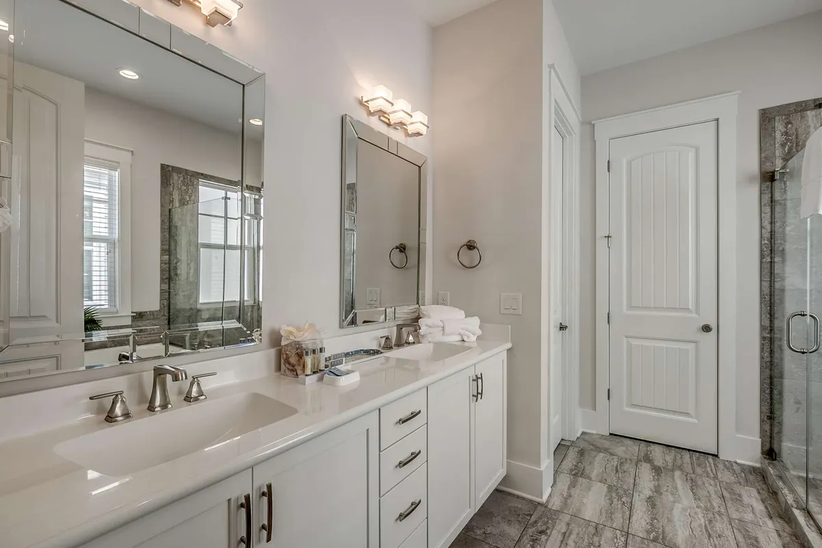 A serene contemporary spa bathroom with a double sink and modern faucets, large mirrors, neatly arranged soft towels, and a stylish glass shower enclosure. The mood is peaceful and organized, perfect for self-care routines and relaxation.