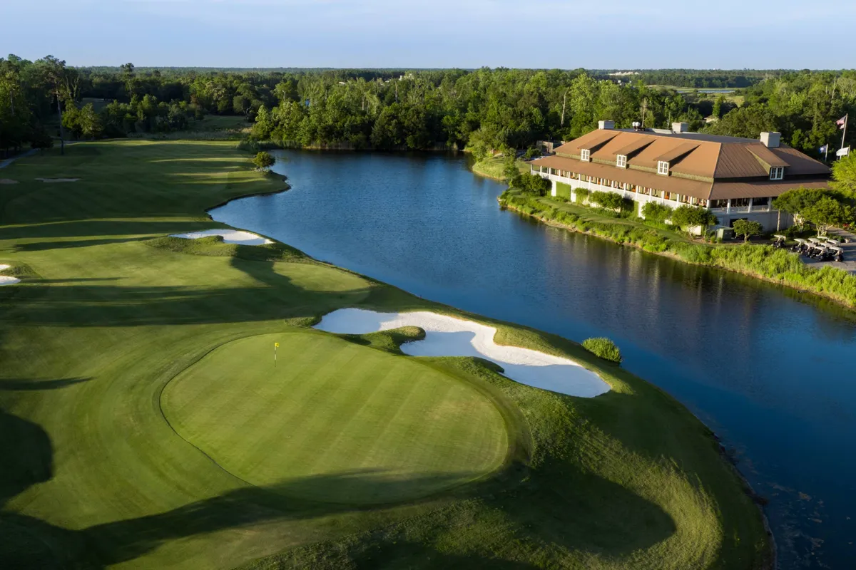 A lush golf course is showcased with a manicured green, tranquil water feature, and a prominent clubhouse in the background. Golfers can be seen enjoying the serene setting, while others relax near the water, underscoring a leisurely atmosphere ideal for recreation and relaxation.