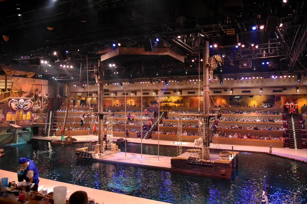 An interior shot of a vibrant theater with a stage set for a water-themed performance, audience seating filled, and theatrical decorations that suggest immersive, family-friendly entertainment.